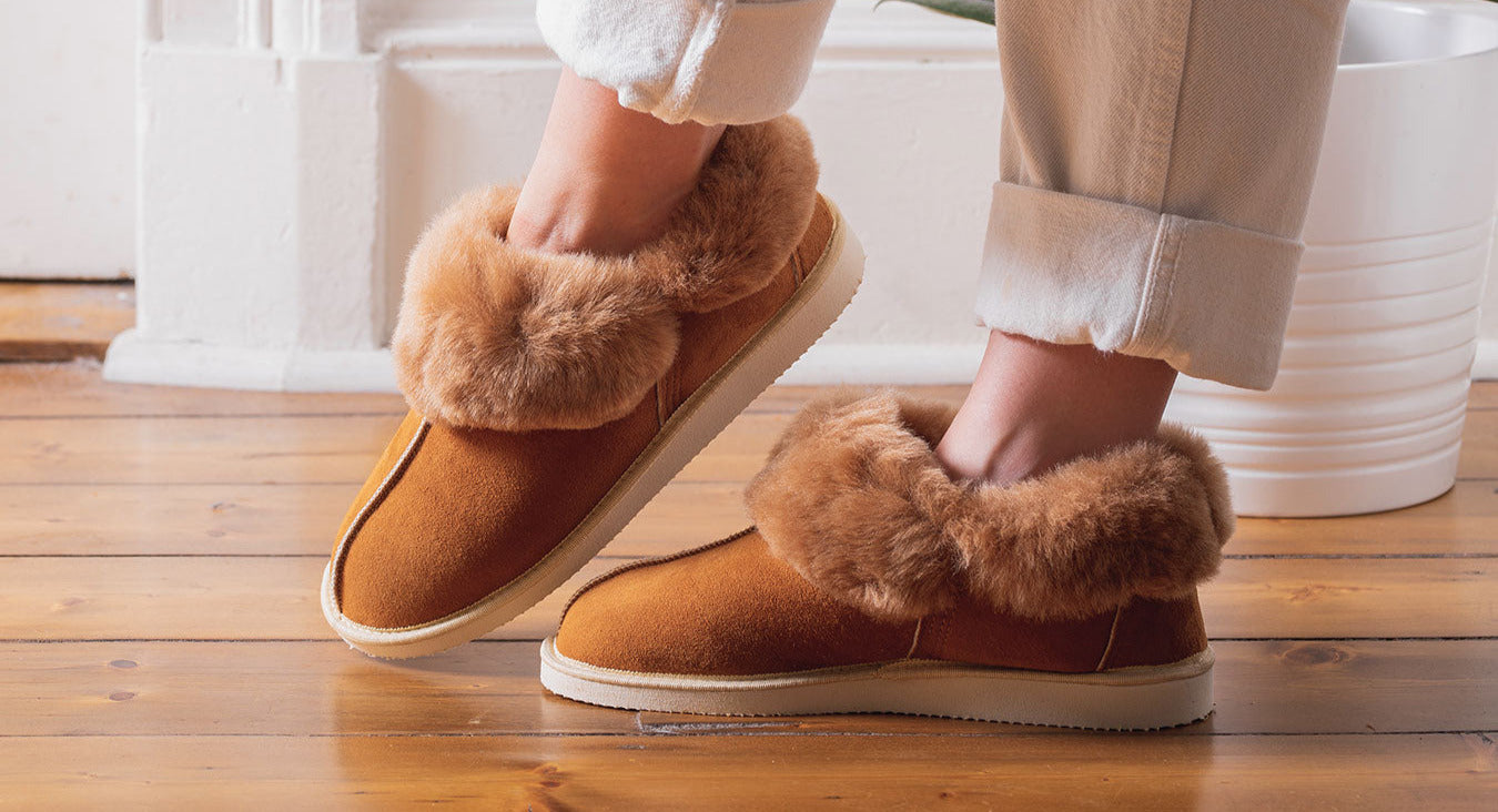 Brown slippers with fur trim worn indoors on a wooden floor.